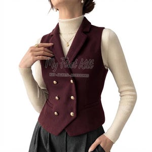 Könnte beinhalten: Eine ärmellose bordeauxrote Weste mit doppelreihiger Vorderseite, sechs goldfarbenen Knöpfen, einem steigenden Revers und zwei Seitentaschen. Der Text My First Kilt KILT-JACKETS-ACCESSORIES ist in Weiß auf der Vorderseite aufgedruckt.