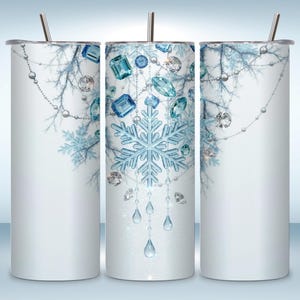 Può includere: Un bicchiere cilindrico in acciaio inossidabile con sfondo bianco e un design a tema invernale. La stampa mostra fiocchi di neve azzurri, gemme pendenti simili a cristalli e delicate catene di perline argentate su rami ghiacciati.