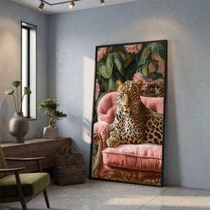 Op de afbeelding: Een ingelijste kunstdruk met een luipaard op een roze fauteuil. De gevlekte vacht van de luipaard contrasteert met de bloemen- en bladerenachtergrond. Het zwarte frame met gouden details geeft het kunstwerk een luxueuze uitstraling.