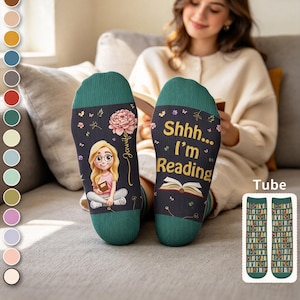 May include: A pair of dark teal socks featuring a cartoon illustration of a blonde person reading a book, a pink flower, and the text "Shhh... I'm Reading" with an open book graphic. A small inset shows a tube sock design with a bookshelf pattern.