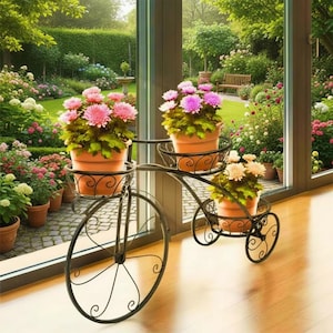May include: A black metal bicycle-style plant stand with three terracotta pots of pink and cream flowers. The stand features a large front wheel and two smaller rear wheels, with decorative scrollwork. The pots are filled with flowers.
