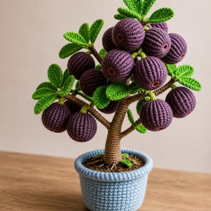 May include: A handcrafted crochet fig tree in a blue pot. The tree features a brown trunk, green leaves, and numerous purple figs. The pot is a light blue color, and the tree is set on a wooden surface.