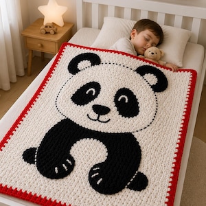 May include: A handmade, crocheted panda bear blanket in black, white, and red. The blanket features a large panda face and body on a white background, with a red border. The blanket is on a bed.