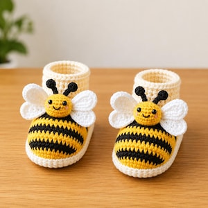 May include: A pair of handmade crochet baby booties. The booties are yellow and black, resembling bees, with white wings and smiling faces. The ankle cuffs are a light cream color.