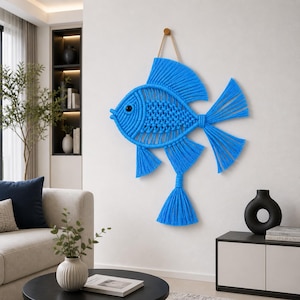 May include: A vibrant blue macrame fish wall hanging. The fish features a detailed woven body, fins, and a tail with fringe. It is suspended from a wooden dowel with a natural fiber cord, adding a touch of coastal decor to any space.