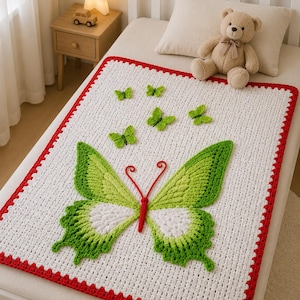 Puede incluir: Una manta blanca de ganchillo con un gran diseño de mariposa verde y blanca y mariposas verdes más pequeñas. La manta tiene un borde rojo y está sobre una cama con un oso de peluche y una almohada.