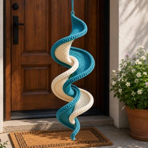 Könnte beinhalten: Eine hängende, spiralförmige Dekoration aus gestricktem Material in abwechselnden Bändern aus Türkis und Creme. Die Spirale hängt an einer dünnen türkisfarbenen Kordel und wird vor einer Holztür präsentiert.