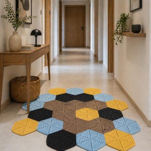 May include: A handmade, hexagonal crochet rug in a hallway. The rug features a geometric pattern with various colors, including yellow, blue, brown, and black. The rug is placed on a light-colored floor, adding a touch of warmth and texture to the space.