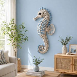 May include: A large, handcrafted seahorse wall decor made of off-white and light blue rope. The seahorse is mounted on a light blue wall, adding a coastal touch to the room. The seahorse measures approximately 30 inches in height.