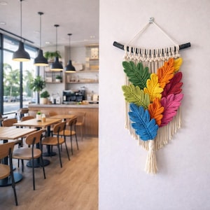 May include: A vibrant macrame wall hanging with a colourful leaf design. The leaves are in shades of blue, green, yellow, orange, and pink, set against a cream-coloured background with a tassel. The wall hanging is displayed against a white wall.