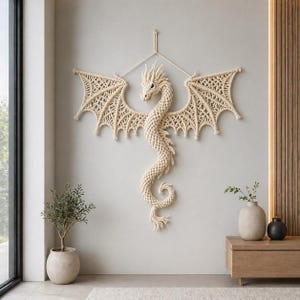 May include: A beige macrame dragon wall hanging with outstretched wings. The dragon features intricate knotwork, a detailed head, and a long, curved tail. The wings are wide and detailed, creating a striking decorative piece.