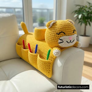 May include: A yellow crochet cat-shaped sofa armrest organizer with a cup holder, pockets, and a tail. The cat has a smiling face with black and white details, and a pink nose. Pens are in the pockets.
