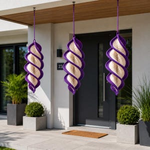 Pode incluir: Três decorações de crochê em espiral suspensas. Cada uma apresenta um centro creme com uma borda roxa. São suspensas do teto por cordas roxas. As decorações estão penduradas em frente a uma casa com uma porta cinza escuro e o número 23.