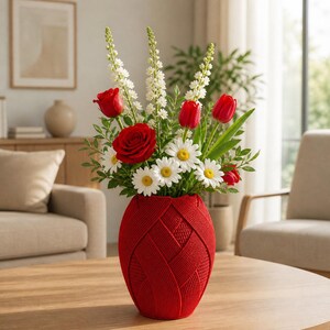 Può includere: Una vivace composizione floreale in un vaso rosso intrecciato. Il bouquet presenta rose rosse, tulipani, margherite bianche e fiori bianchi con foglie verdi. Il vaso è su un tavolo di legno.