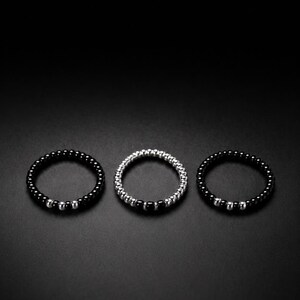 May include: Three circular rings arranged in a horizontal row. The outer two rings consist of small black beads with a segment of silver beads. The centre ring is composed of small silver beads with a segment of black beads.
