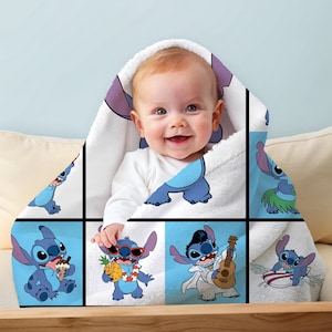 May include: A baby wrapped in a white hooded towel featuring a blue cartoon character. The towel has a grid pattern with the character in various poses, including eating ice cream and playing a guitar. The baby is smiling.