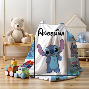 May include: A white fleece blanket featuring a cartoon character with large ears and blue fur. The blanket has the name "Angelina" printed in black. The blanket is surrounded by other cartoon images of the character.