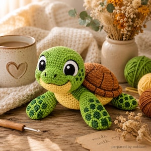 May include: A handmade crochet turtle in shades of green, yellow, and brown. The turtle has large, friendly eyes and a smiling face. The image includes a mug, yarn, and a note that says "made with love".