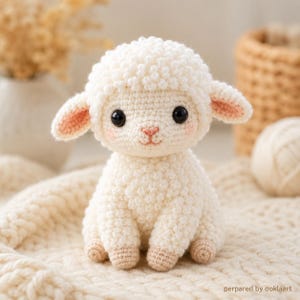 May include: A crocheted lamb toy, featuring a fluffy, cream-coloured body, large black eyes, and pink detailing on the ears and cheeks. The lamb is seated on a cream knitted blanket. A charming, handmade animal.