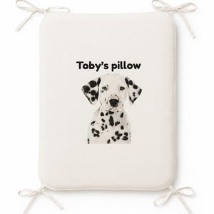 May include: A rectangular off-white seat cushion with four corner ties. The center features a graphic illustration of a Dalmatian puppy with black spots and the black text Toby's pillow printed above the dog's head on the fabric surface.