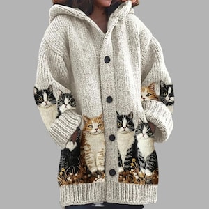 May include: A long-sleeved, hooded knit cardigan in a light heather gray color. The garment features a button-down front closure and a repeating graphic print of various cats along the lower section, including tabby, black and white, and calico.