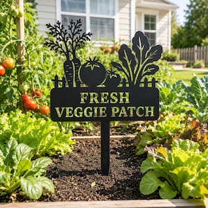 Puede incluir: Un letrero de jardín de metal negro con una silueta de zanahorias, tomates y verduras de hoja sobre un cartel rectangular con el texto recortado FRESH VEGGIE PATCH. El cartel está montado sobre un poste vertical para insertar en tierra.