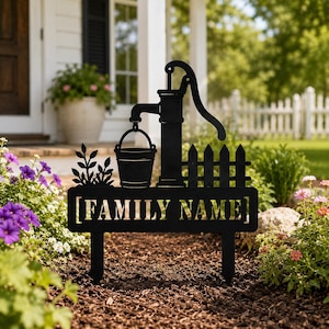 Pode incluir: Uma estaca de jardim de metal preto com a silhueta de uma bomba de água, um balde, uma pequena cerca e uma planta. O design inclui uma base retangular com o texto [FAMILY NAME] recortado em um estilo de fonte em letras maiúsculas.