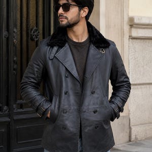 May include: A black leather jacket with a faux fur collar. The double-breasted jacket has two rows of buttons, belt detailing on the sleeves, and pockets. The jacket is worn with a dark sweater and blue jeans.