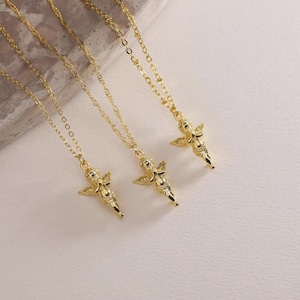 May include: Three gold necklaces, each with a cherub pendant. The necklaces have fine chains and detailed cherub charms with wings. The jewellery is displayed on a light-coloured surface.