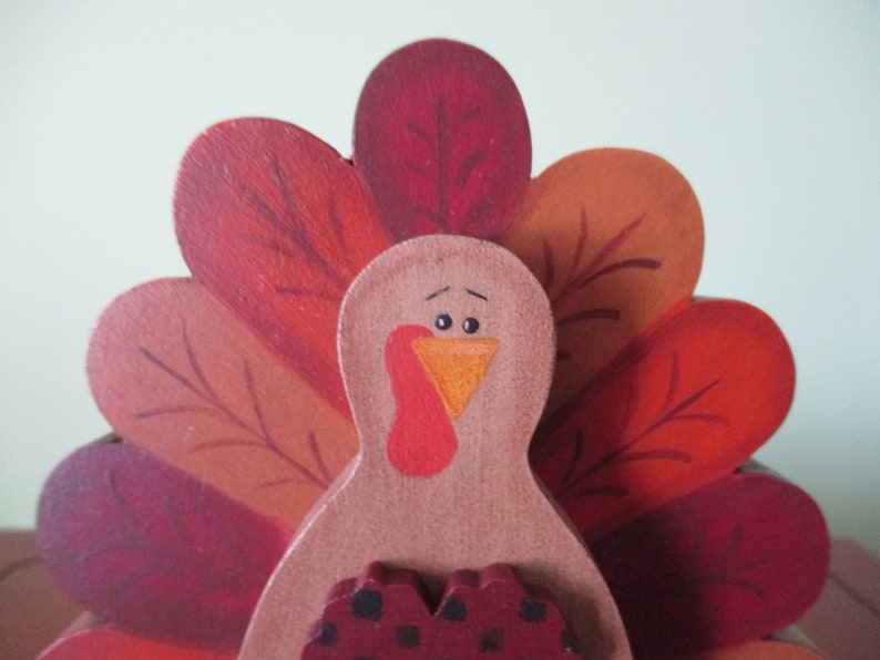 Op de afbeelding: Houten kalkoenfiguur met een rood, oranje en bruin geschilderde staartveren. De kalkoen heeft een bruin lichaam, een rode keelzak en een oranje snavel.