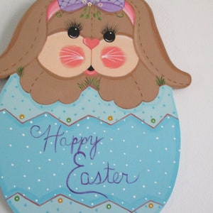 May include: A painted wooden Easter bunny with a purple bow and a blue egg with white polka dots. The egg says "Happy Easter" in purple paint.