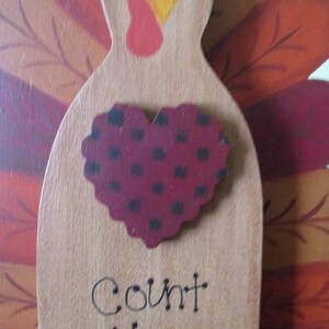 Op de afbeelding: Houten kalkoenfiguur met een rood hart met zwarte stippen en het woord "Count" eronder. De kalkoen heeft bruine, oranje en rode veren.