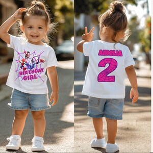 May include: A white t-shirt with a Spider-Man graphic and the text "BIRTHDAY GIRL" in pink. The back of the shirt has the name "AMELIA" and the number "2" in pink. The outfit includes denim shorts and white trainers.