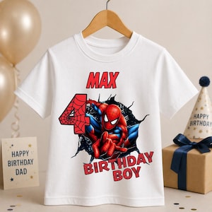May include: White t-shirt featuring a graphic of Spider-Man bursting through a wall, with the name "MAX" and the number "4" in red. The text "BIRTHDAY BOY" is also in red. A fun birthday shirt.