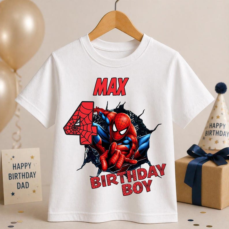 May include: White t-shirt featuring a graphic of Spider-Man bursting through a wall, with the name "MAX" and the number "4" in red. The text "BIRTHDAY BOY" is also in red. A fun birthday shirt.