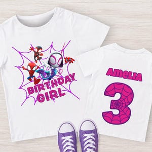 May include: White t-shirts with a Spider-Man theme. One shirt features a purple spiderweb design with the words "BIRTHDAY GIRL" and Spider-Man characters. The other shirt has the name "Amelia" and the number "3" in pink.