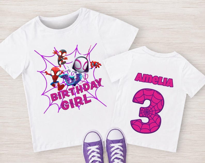 May include: White t-shirts with a Spider-Man theme. One shirt features a purple spiderweb design with the words "BIRTHDAY GIRL" and Spider-Man characters. The other shirt has the name "Amelia" and the number "3" in pink.