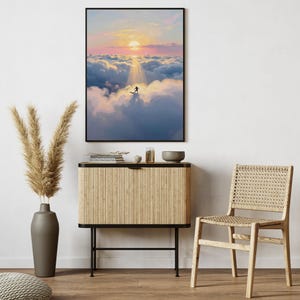 May include: A framed art print depicts a surfer riding a wave above the clouds, bathed in the golden light of a sunset. The artwork is displayed above a wooden cabinet with a vase of pampas grass and a woven chair.