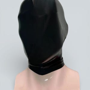 Puede incluir: Una capucha de látex negro con una superficie lisa y brillante. La capucha cubre toda la cabeza y el cuello, con un escote definido. El material es ajustado y opaco, creando una estética elegante y minimalista.