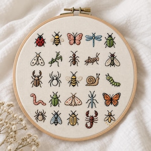 Op de afbeelding: Een ronde houten borduurring met een wit stoffen paneel voorzien van vijfentwintig verschillende handgeborduurde insecten- en kleine diermotieven, waaronder een lieveheersbeestje, bijen, vlinders, een slak, een rups en een schorpioen.