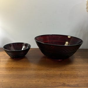 Puede incluir: Dos cuencos de cristal rojo oscuro de diferentes tamaños, ambos con un patrón de diamantes texturizado en el exterior. Los cuencos tienen un acabado translúcido y una forma redondeada, siendo uno significativamente más grande que el otro.