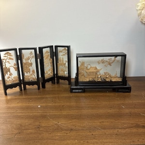 May include: A four-panel folding screen and a rectangular display case, both featuring black frames and intricate light-colored cork carvings depicting landscapes with pagodas, trees, and rock formations behind glass panels.