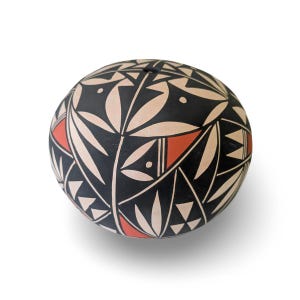 May include: A spherical ceramic vessel featuring a matte finish with a complex geometric pattern in black, cream, and terracotta red. The design consists of repeating leaf-like shapes, triangles, and fine lines covering the entire rounded surface.