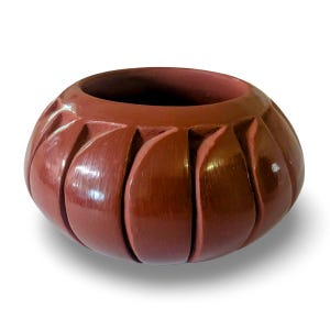 May include: A round, terracotta-colored ceramic bowl featuring a series of vertical, carved grooves that create a petal-like, segmented appearance around the exterior. The surface has a smooth, polished finish with a deep reddish-brown hue.