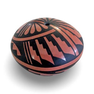 May include: A rounded, low-profile ceramic vessel featuring a terracotta and black geometric pattern. The design includes radiating petal-like shapes at the top center, surrounded by repeating stepped, angular motifs that wrap around the body.