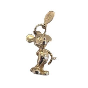 Pode incluir: Um berloque do Mickey Mouse dourado. O berloque &eacute; uma figura tridimensional do Mickey Mouse, com suas orelhas, cal&ccedil;as curtas e luvas caracter&iacute;sticas. O berloque tem uma pequena argola na parte superior para prender a um colar ou pulseira.