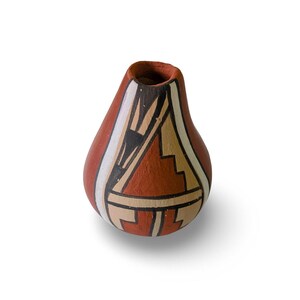 May include: A small, teardrop-shaped terracotta vase featuring a matte finish. The surface is decorated with hand-painted geometric patterns in black, white, and tan, arranged in stepped and linear designs against the natural reddish-brown clay base.