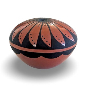 May include: A rounded terracotta pottery vessel featuring a small circular opening at the top. The surface is decorated with a black painted pattern of radiating petals around the rim and a scalloped band encircling the lower section.