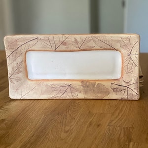 May include: A rectangular ceramic serving dish with a white interior and a beige exterior. The beige exterior is decorated with leaf imprints. The dish is likely used for serving appetizers or small dishes.