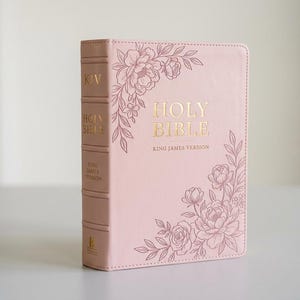 Può includere: Una Sacra Bibbia rosa, versione King James, con scritte dorate e illustrazioni floreali. La copertina presenta le parole "Holy Bible" e "King James Version". Il dorso mostra "KJV" e "Holy Bible".